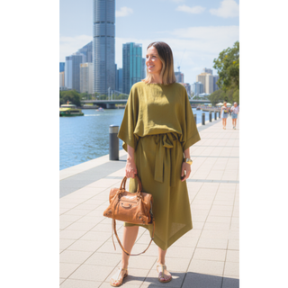 Woman in olive kimono dress with a belt standing by a river in a cityscape, showcasing a modern kimono style.