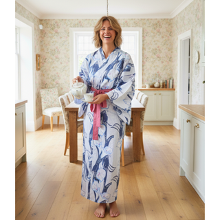 Woman wearing a yukata sewing pattern in a cozy kitchen, holding a teapot and smiling.